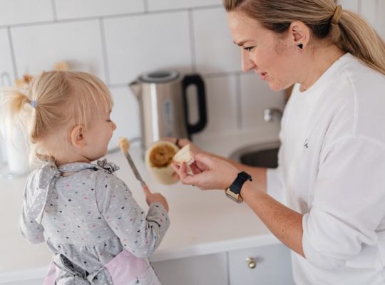 A mother and her young daughter interact while preparing food in a modern kitchen.