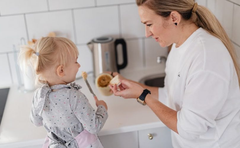 A mother and her young daughter interact while preparing food in a modern kitchen.